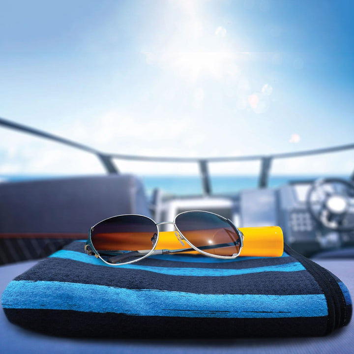 Bondi blue beach towel folded on seat of a speed boat with sunglasses and sunscreen placed on top.