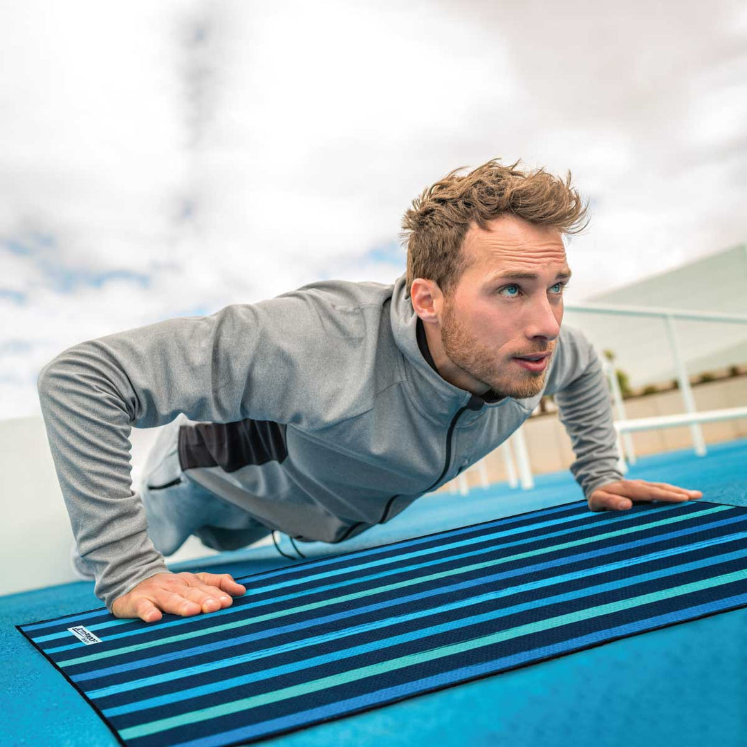 Blonde hair blue eyed man doing push up over striped antibacterial teal gym towel