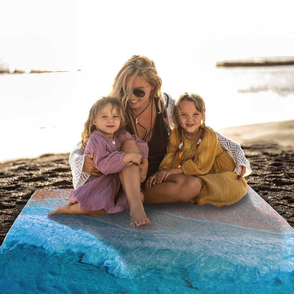 Beautiful blond mother with two young children happy together sitting on the shore on an oversized Sand- Free Towel