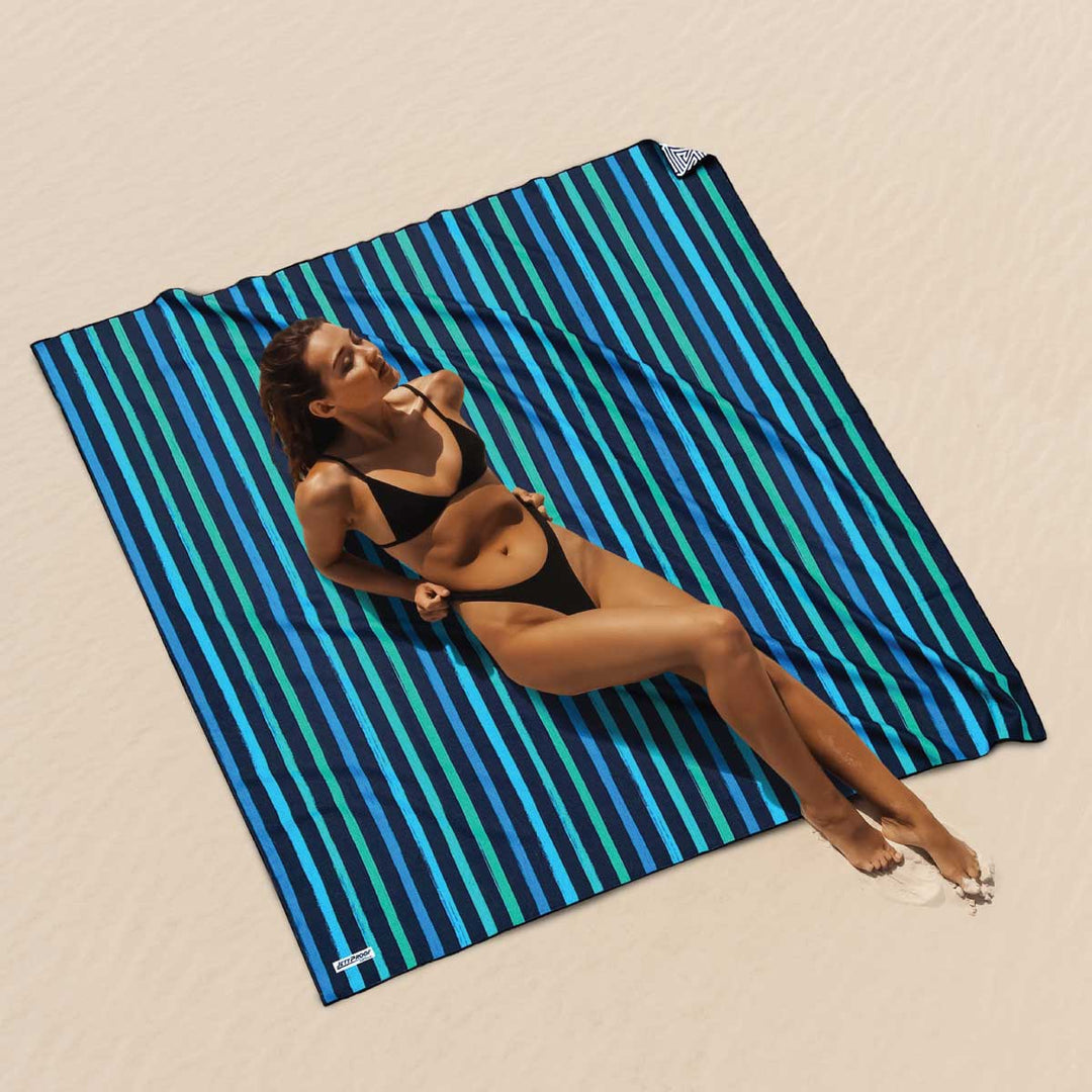 beautiful fit women sunbaking on undisturbed sand , leaning back on oversized sand free beach towel