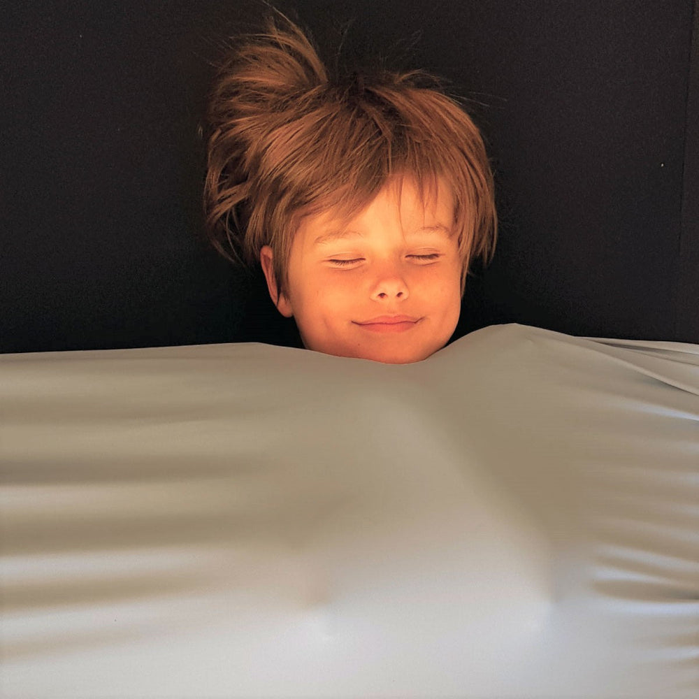 Happy boy snuggled into light gray compression sheet with Black fitted sheet by JettProof